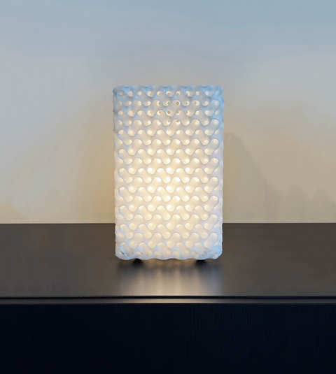 Schwarz Minimal Surface #1 table lamp lit on a dark sideboard — the white Schwarz lattice glowing warm from within