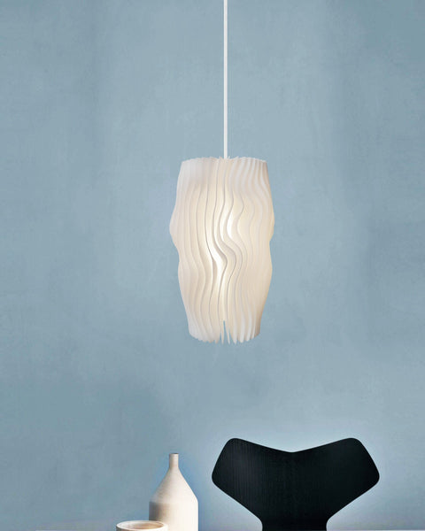 Morandi Lamella #1 pendant light glowing against a powder-blue wall above ceramic vases and a black chair