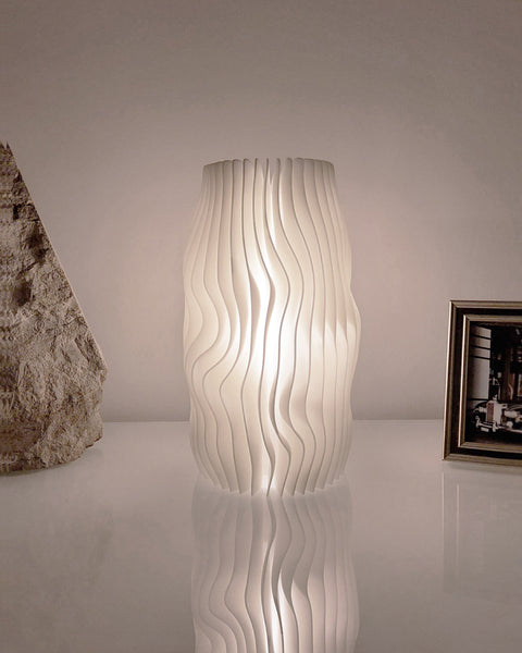 Morandi Lamella #1 table lamp lit on a white table between a stone object and a framed photo
